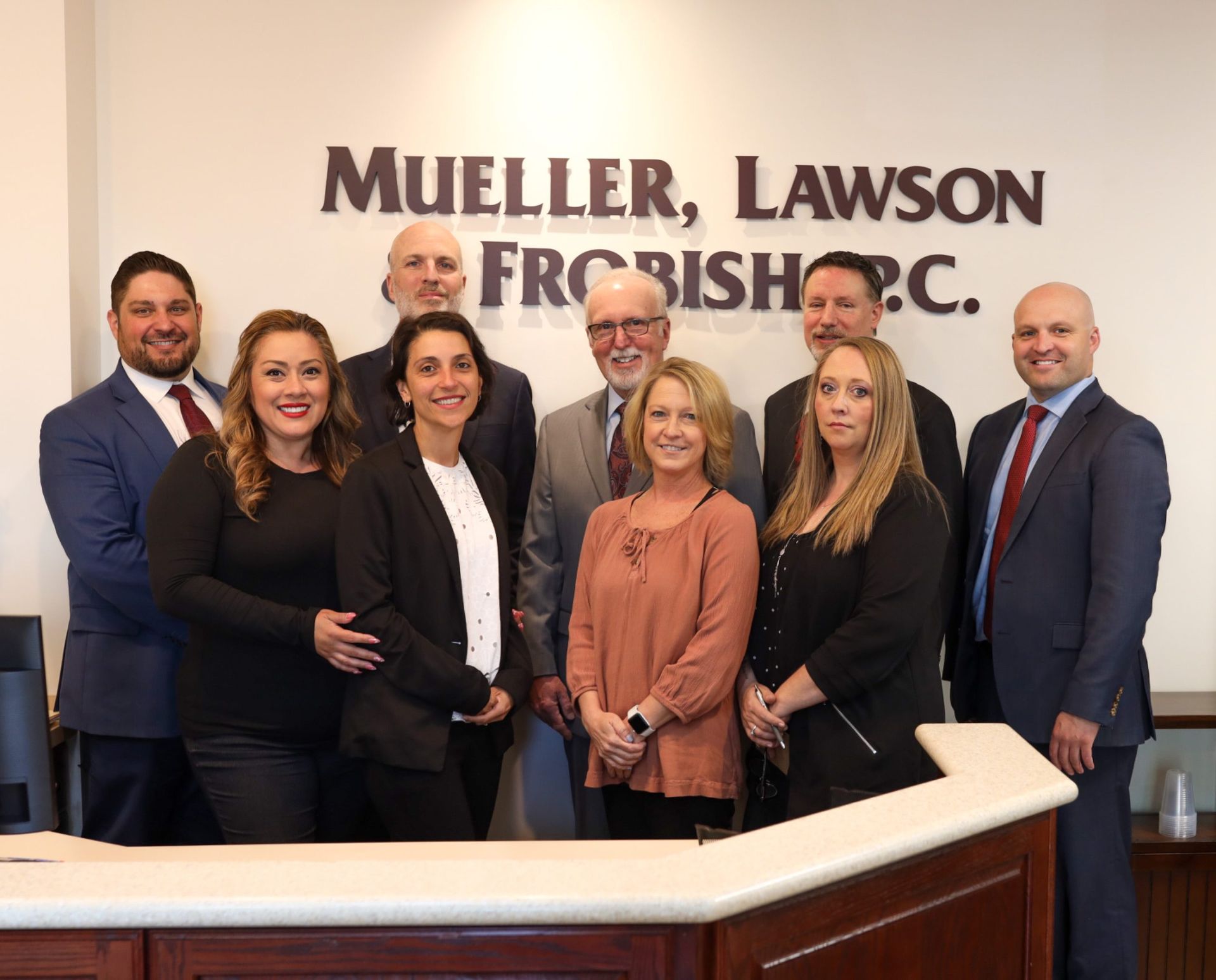 Group of lawyers standing in front of their law firm's sign, with a reception desk in front. Group of lawyers standing in front of their law firm's sign, with a reception desk in front.