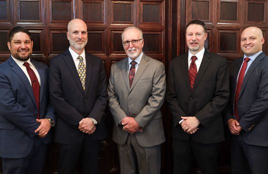 Five men in suits standing in front of a wooden door. They all smile, and wear ties. Five men in suits standing in front of a wooden door. They all smile, and wear ties.