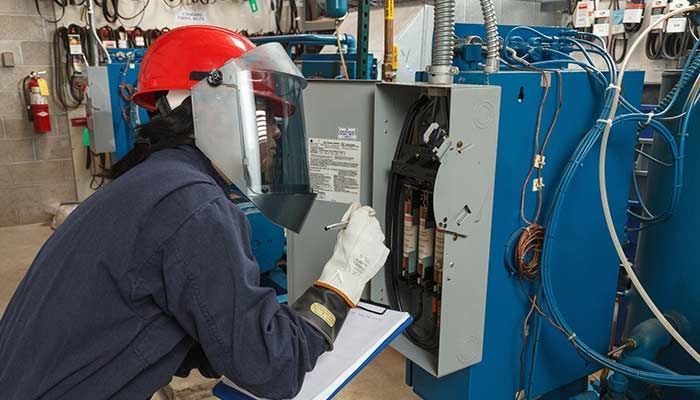 Person wearing protective gear inspecting electrical panel.