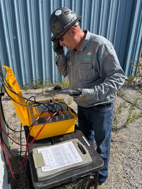 Man in hard hat examines electrical equipment outdoors.
