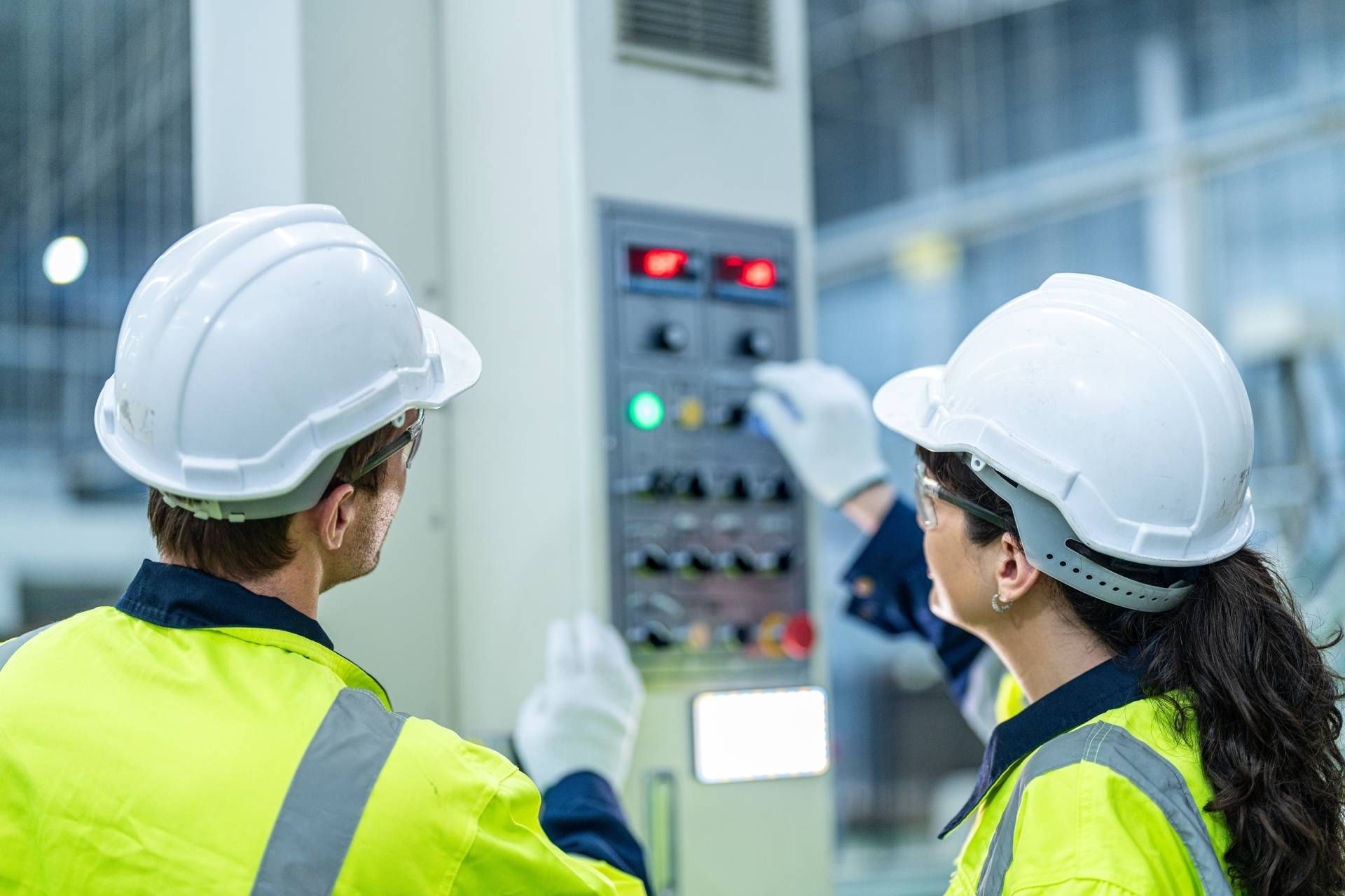 Two professionals wearing white hard hats, gloves, and bright safety vests performing an equipment i