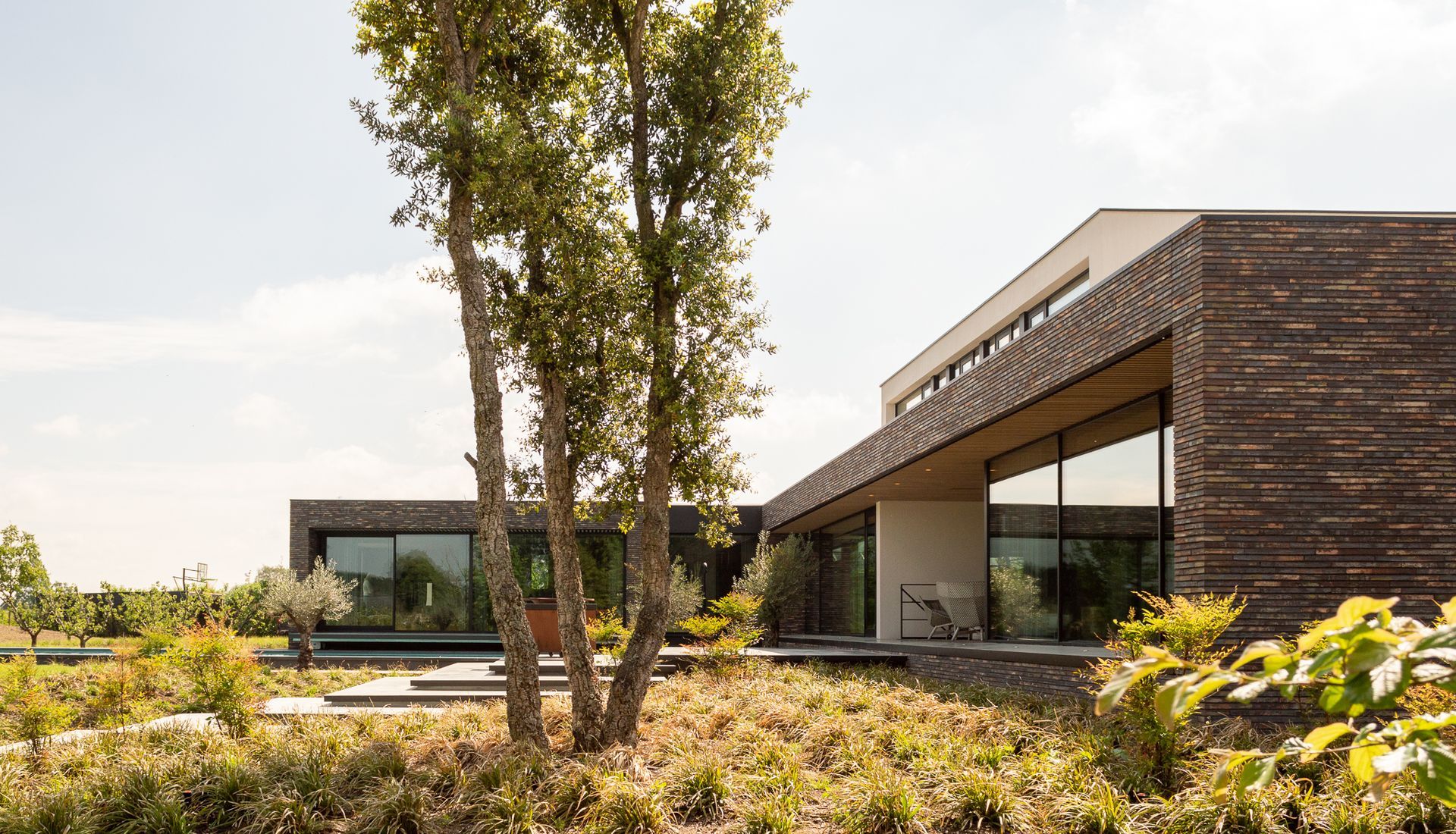 Een modern huis met veel ramen en bomen ervoor.