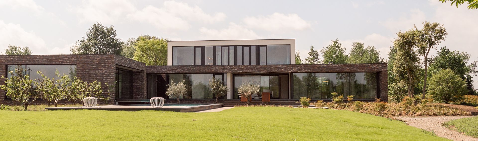 Een villa met veel ramen, omgeven door bomen en gras.