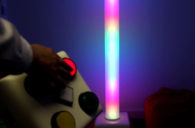 A tall, vertical tower lamp glows with four bright blue lights against a dark wall in a dimly lit room.