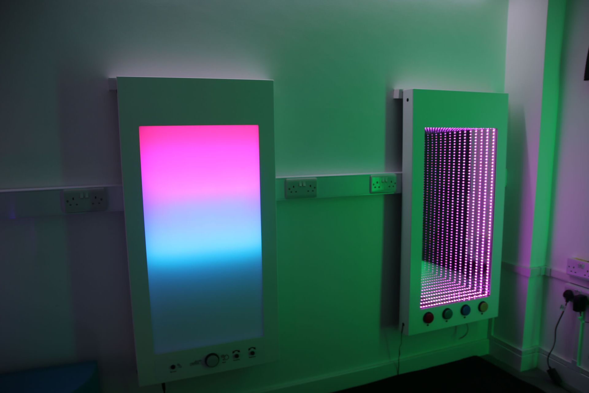 Two illuminated vertical bubble tubes and a glowing, multi-colored panel light in a dimly lit sensory room.