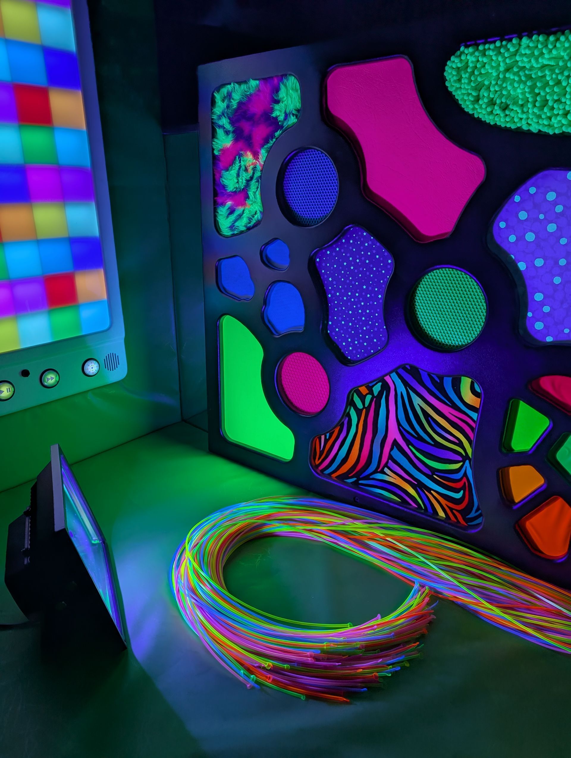 A black frame filled with vibrant, neon-colored patterns and shapes illuminated by a UV light, with coiled tubing below.