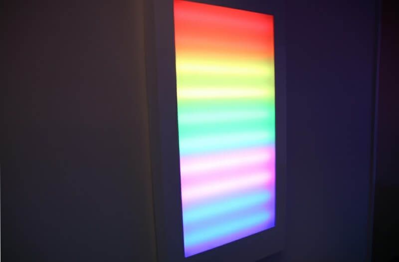 A vertical, glowing rainbow panel stands next to a projected scene of several hot air balloons in a dimly lit room.