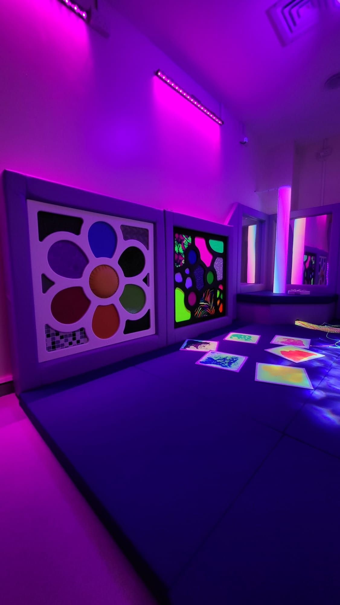 A square sensory board with a central yellow circle surrounded by six colorful, textured, petal-shaped fabric patches.