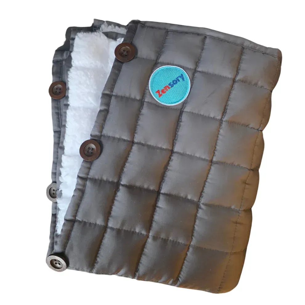 A grey, quilted sensory blanket with a soft white lining and brown button closures, featuring a blue circular logo.