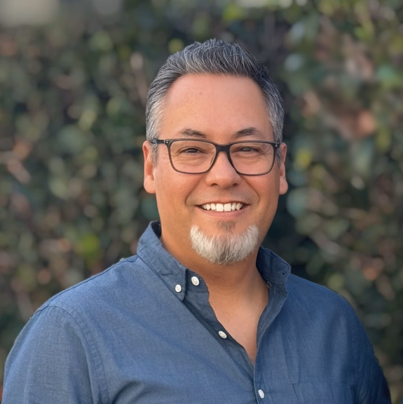 A man wearing glasses and a plaid shirt is smiling for the camera.