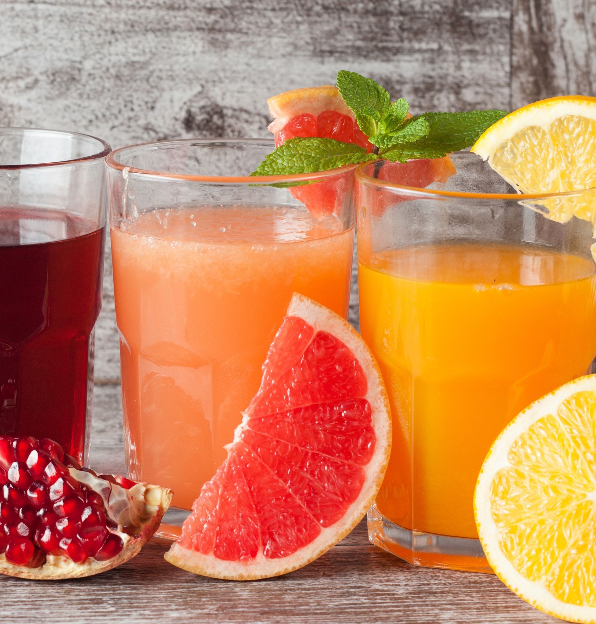 Assorted fruit juices with grapefruit, orange, lemon, and pomegranate on a rustic table Assorted fruit juices with grapefruit, orange, lemon, and pomegranate on a rustic table