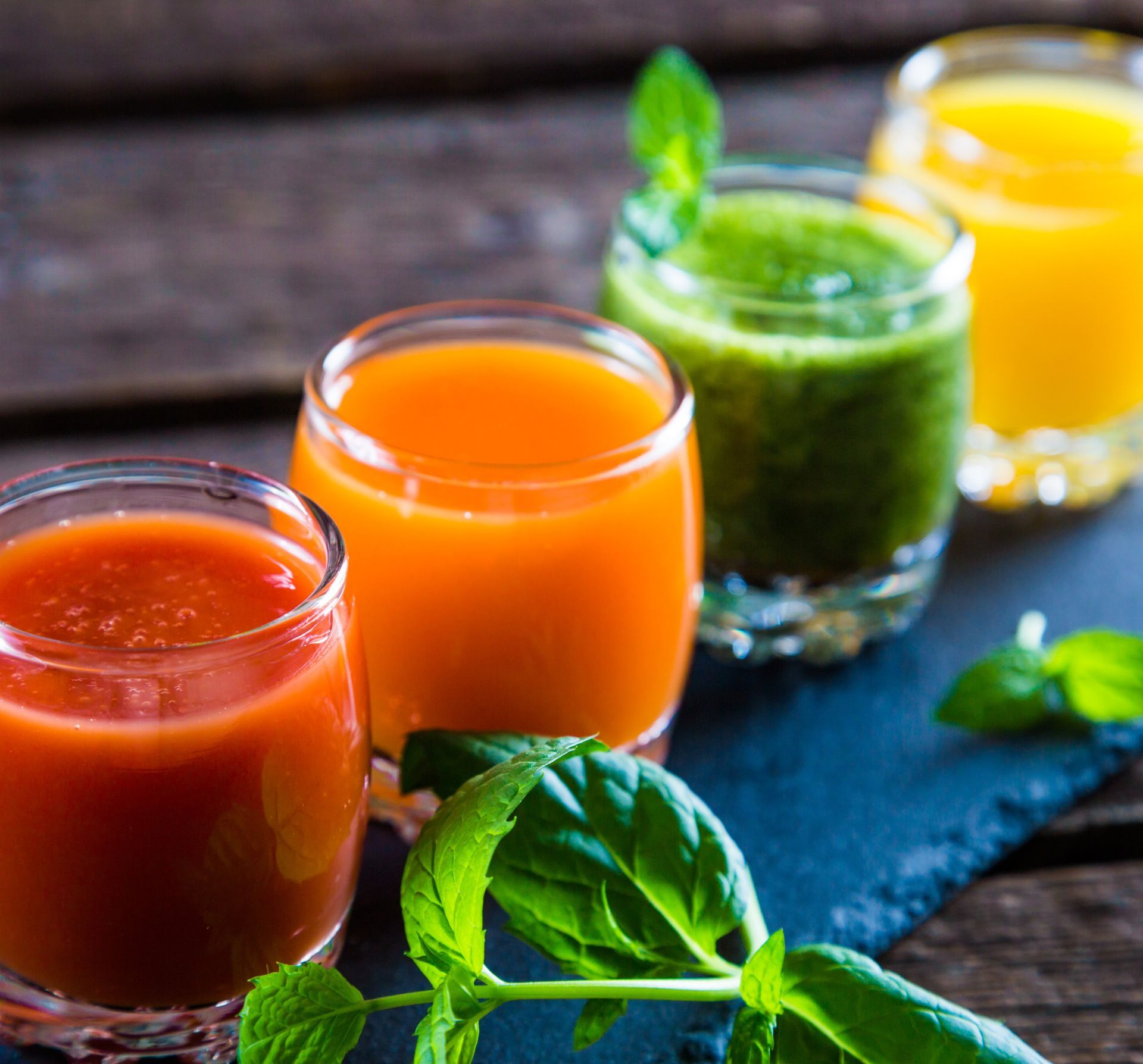 Four colorful fruit juice in glasses on a dark table with mint leaves Four colorful fruit juice in glasses on a dark table with mint leaves