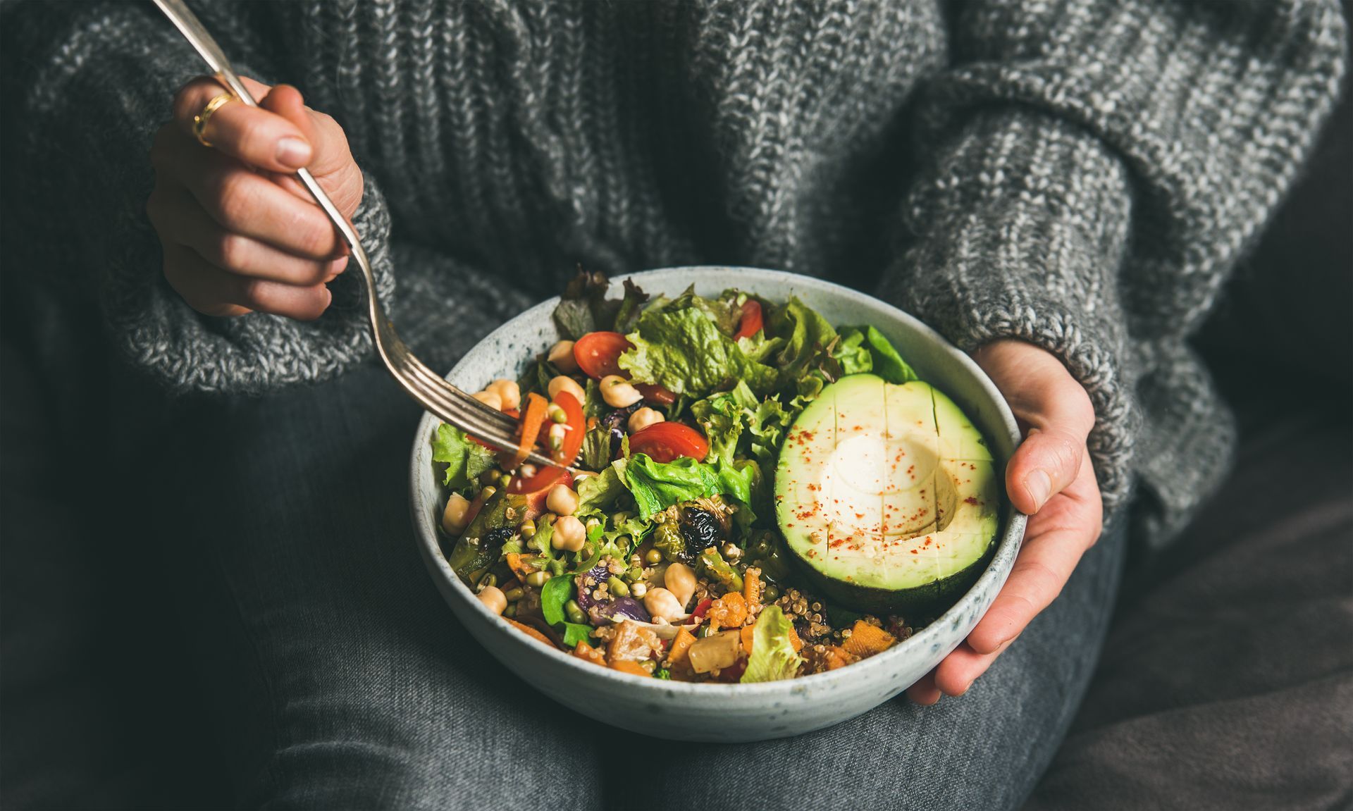 Woman in jeans and warm sweater holding bowl with fresh salad.