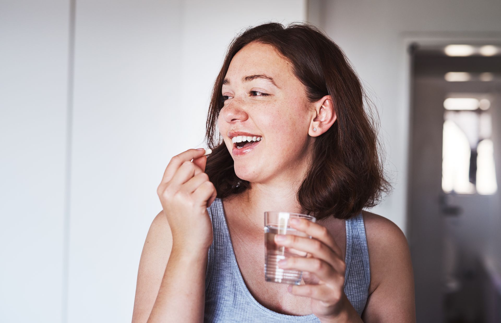 Person taking a pill with a glass of water indoors.