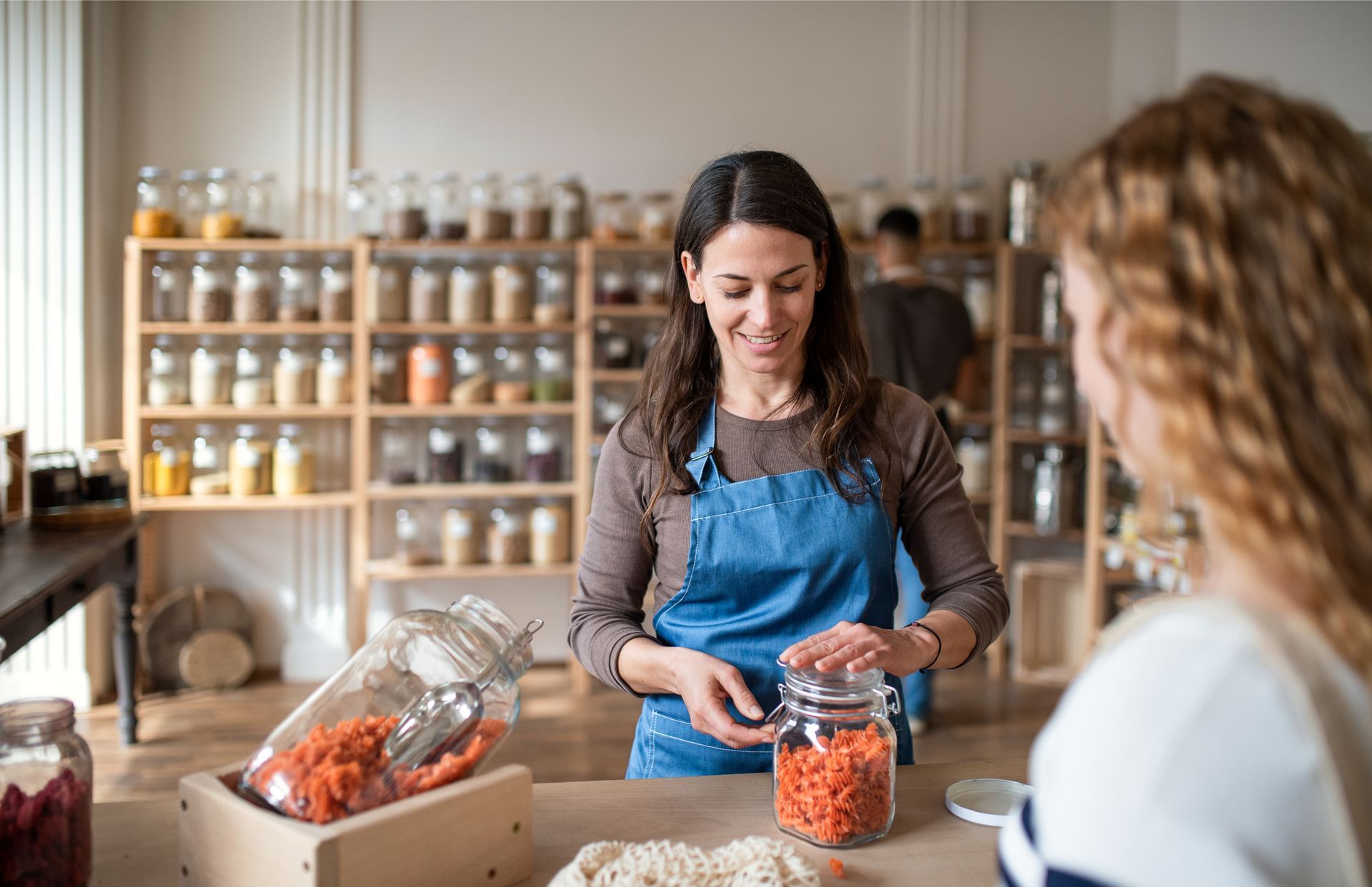 Woman shop assistant working in zero waste shop, serving customer.