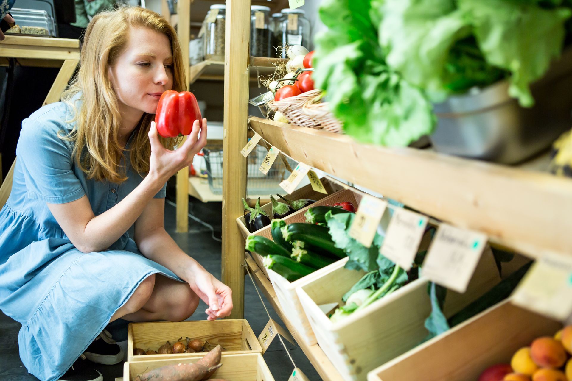 Person in blue dress holding red pepper in grocery store. Person in blue dress holding red pepper in grocery store.