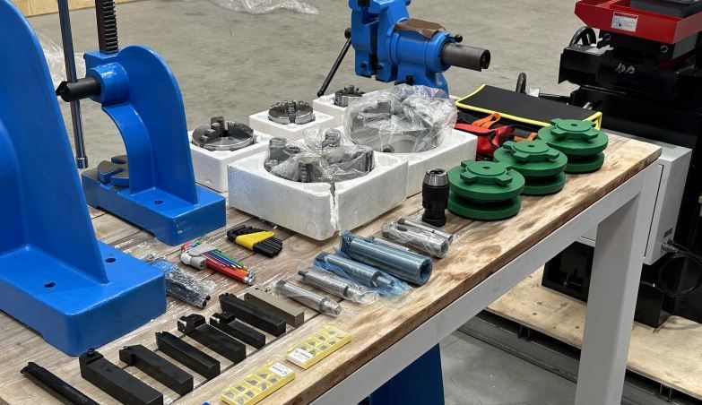 Workbench with blue pipe-clamp tools, green fittings, and metal parts laid out on a table in a workshop.