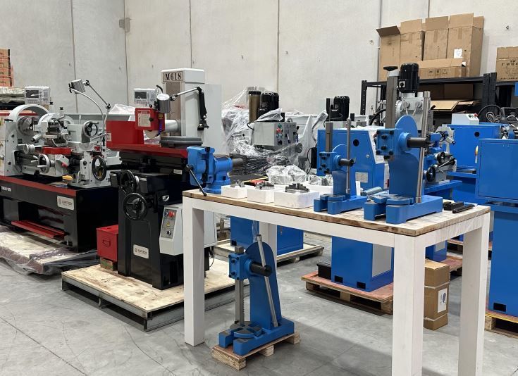 Industrial workshop with red and blue machinery on pallets and a white worktable in front