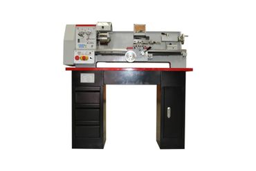 Metal lathe on a black workbench in a workshop, with drawers below and tools mounted above