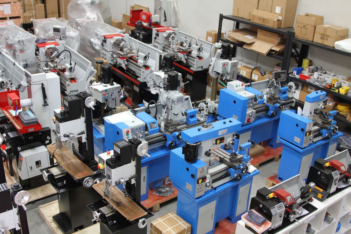 Rows of blue and silver industrial machines in a workshop, surrounded by boxes and equipment.