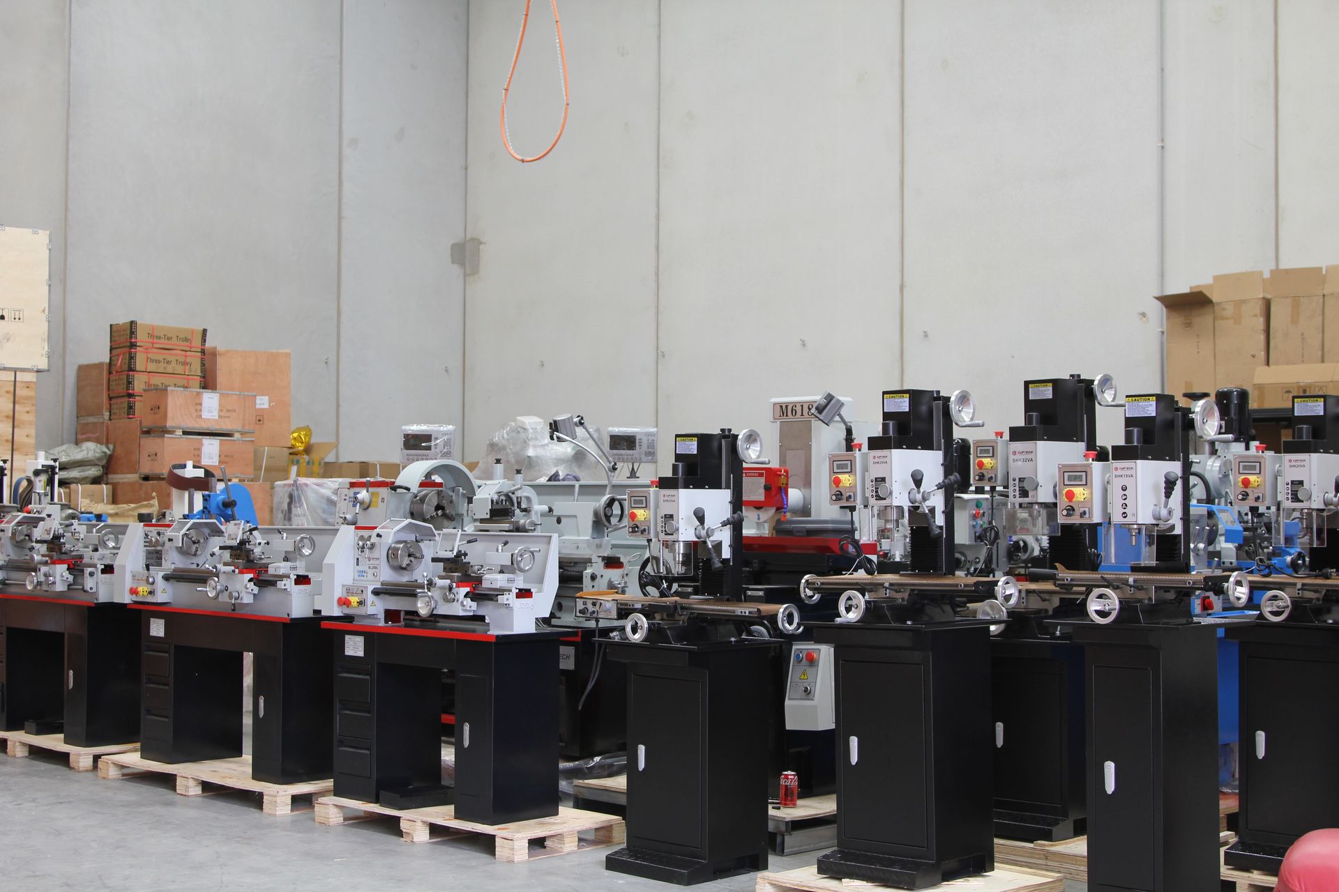 Rows of black industrial machines in a warehouse, with boxes and equipment stacked along the back wall.