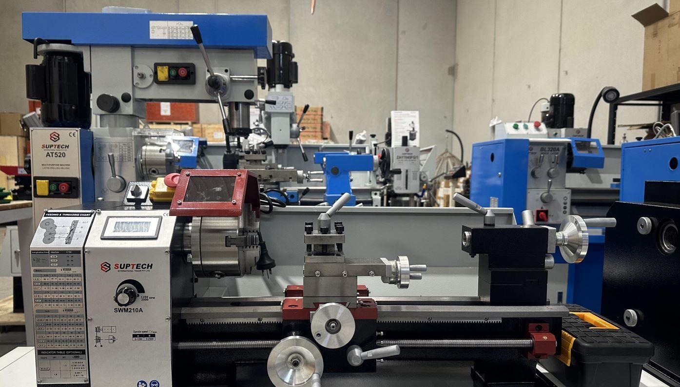 Machine shop with a gray metal lathe in front and blue industrial machinery in the background.