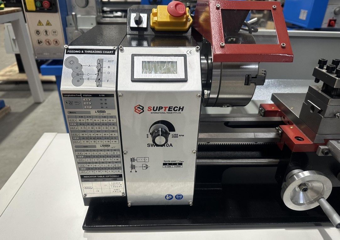 Small metal lathe in a workshop, with control panel, handwheel, and red emergency stop button.