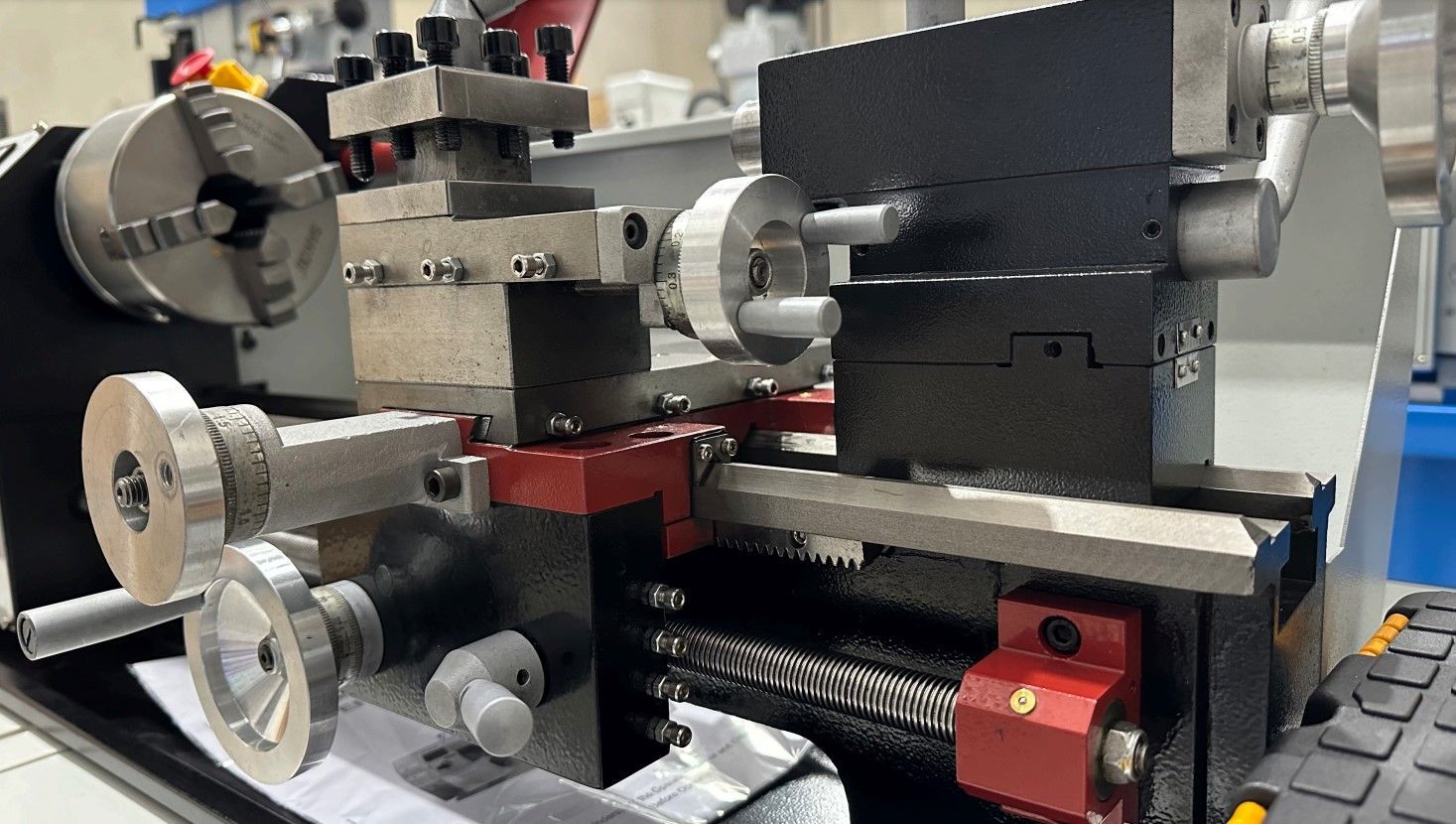 Close-up of a metal lathe with silver knobs, black housing, and red components in a workshop.
