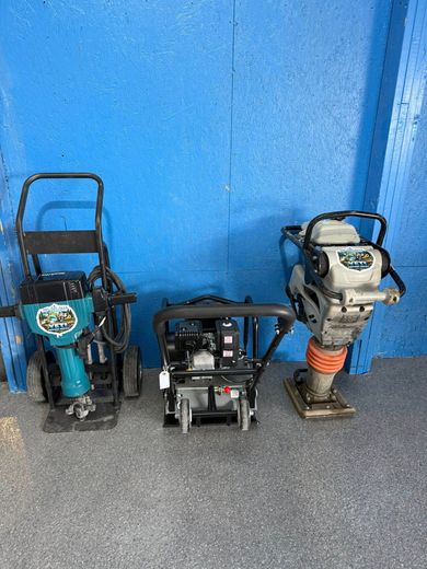 Three construction tools on a gray floor against a blue wall, including two compactors and a small machine.