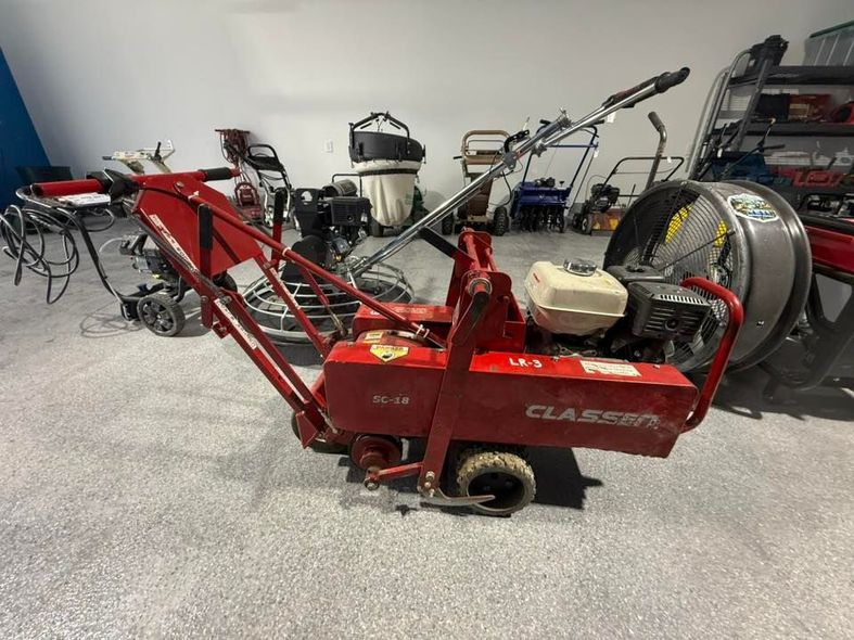 Red Claas farm machine with pickup reel in a workshop, surrounded by other equipment.