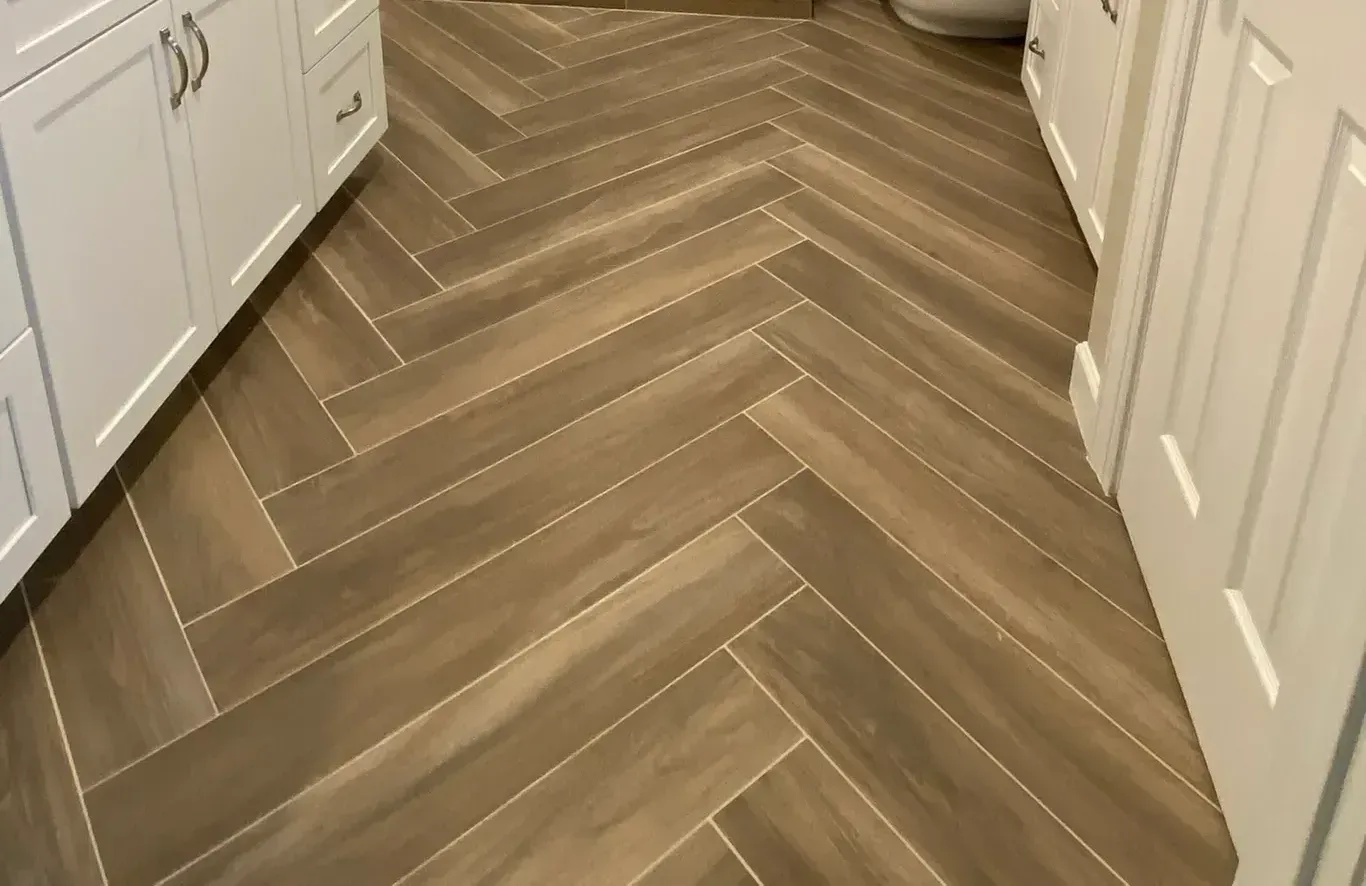 A bathroom with a herringbone tile floor and white cabinets.