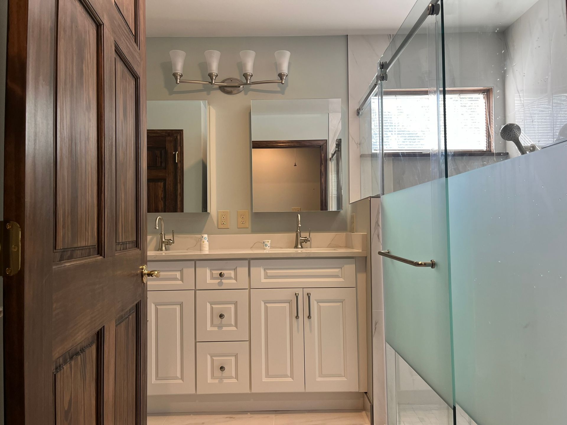 A bathroom with two sinks , a mirror , and a walk in shower.