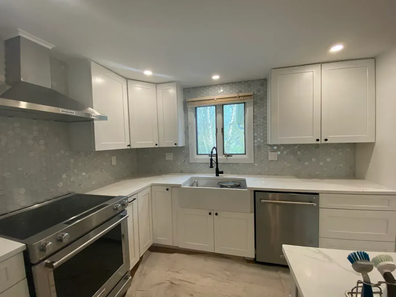 A kitchen with white cabinets , stainless steel appliances , a sink and a window.