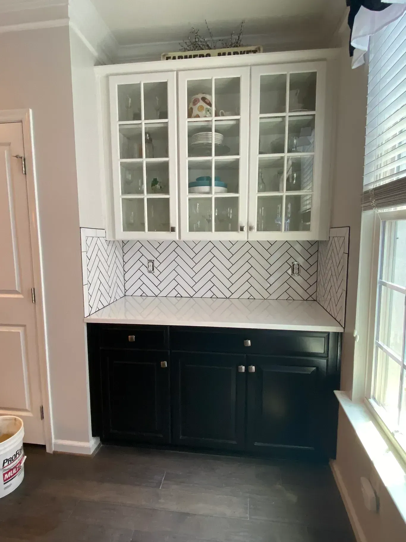 A kitchen with black cabinets and white counter tops and a window.