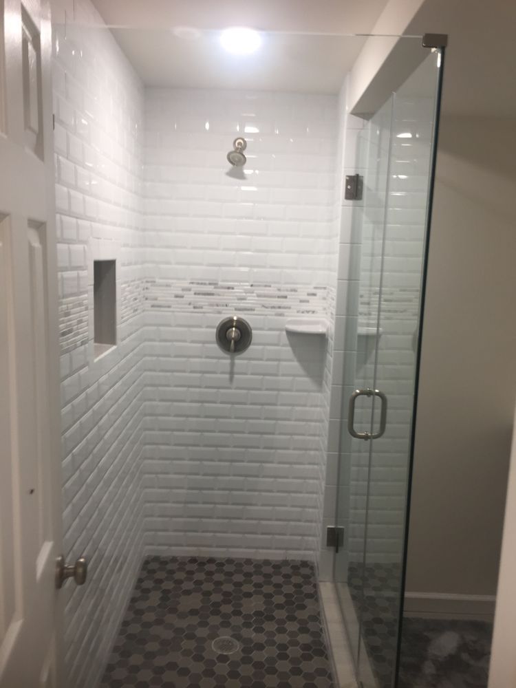 A bathroom with a walk in shower with white tiles and a glass door.