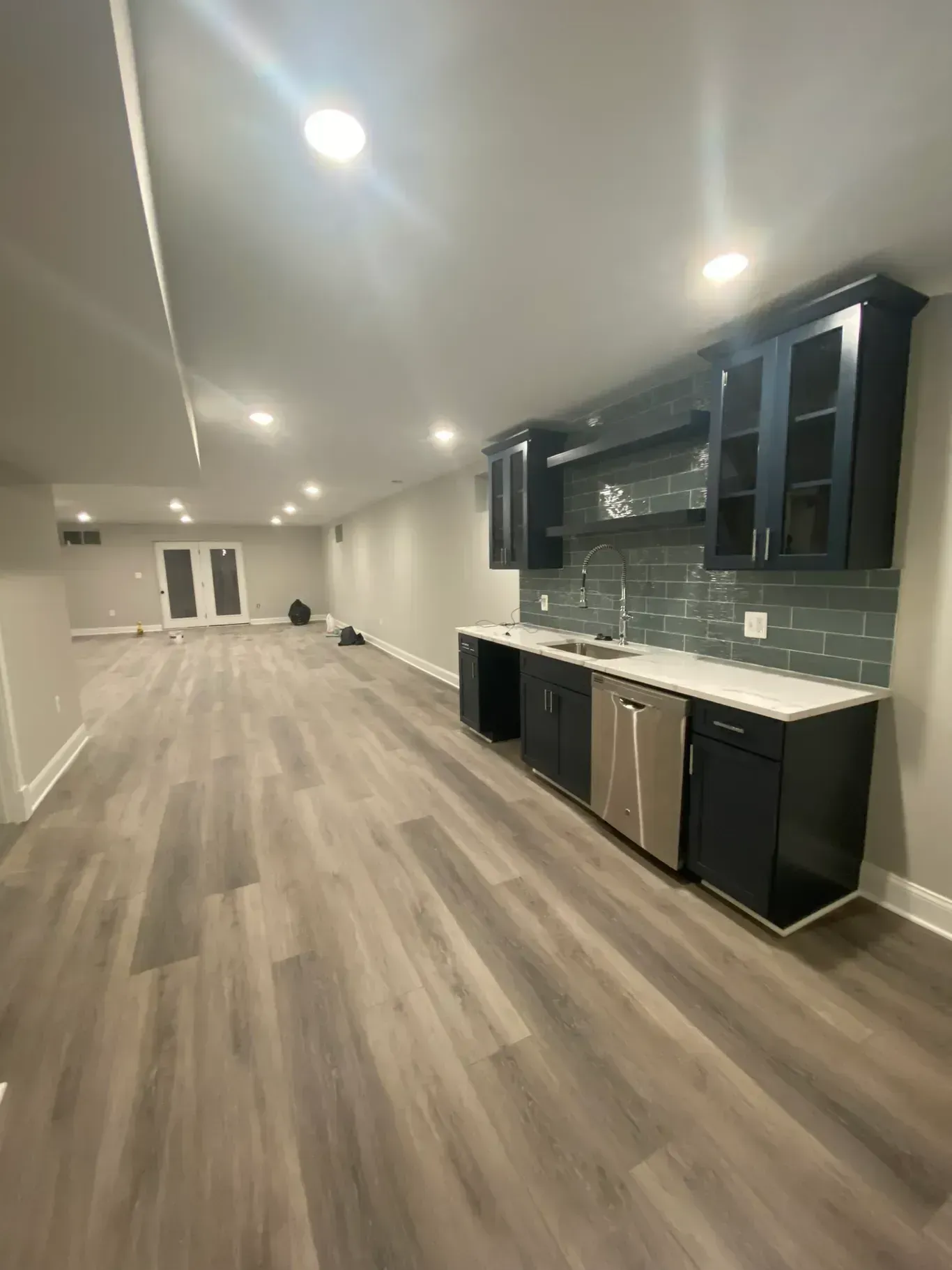 A kitchen in a basement with hardwood floors and black cabinets.