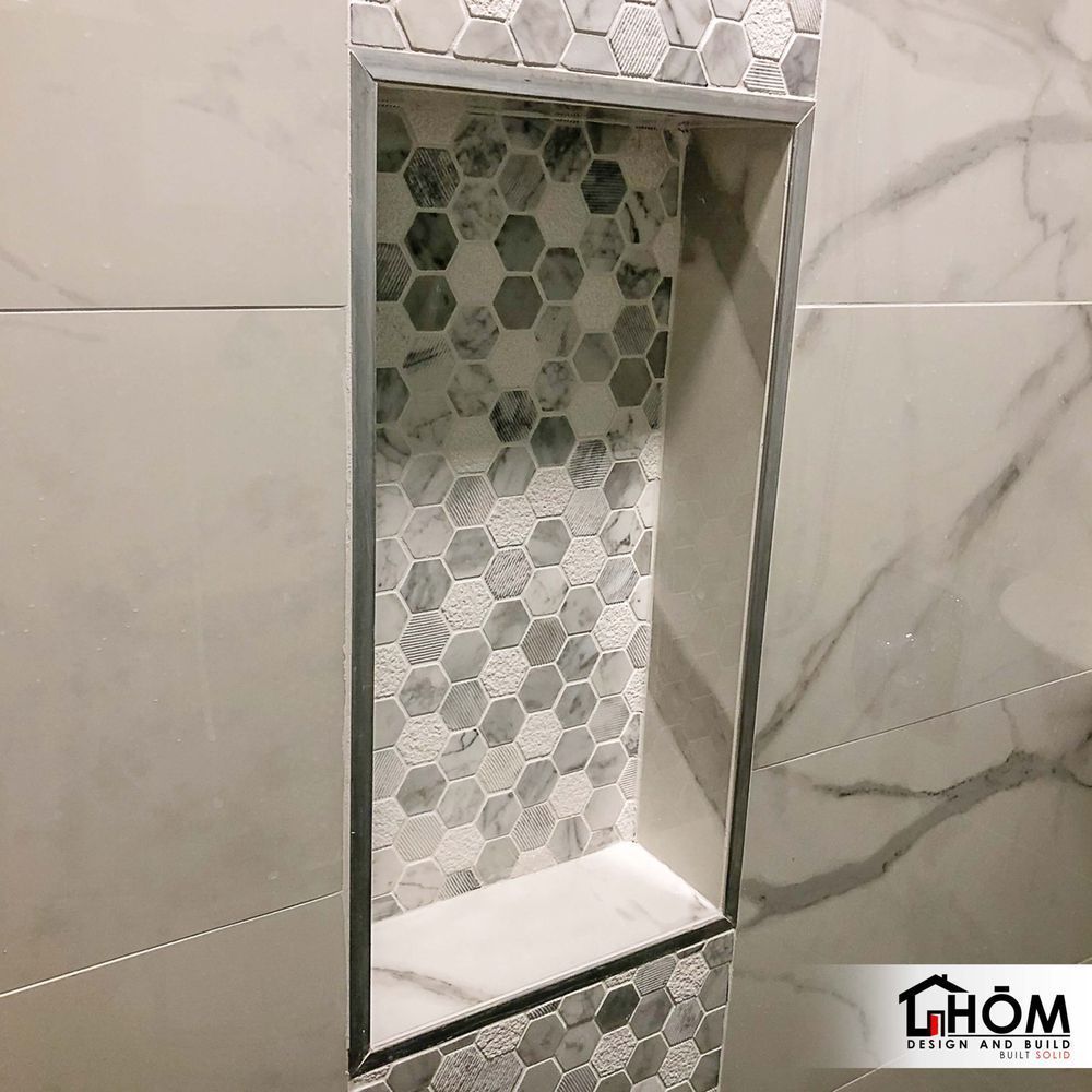 A shower niche in a bathroom with marble tiles and a stainless steel frame.