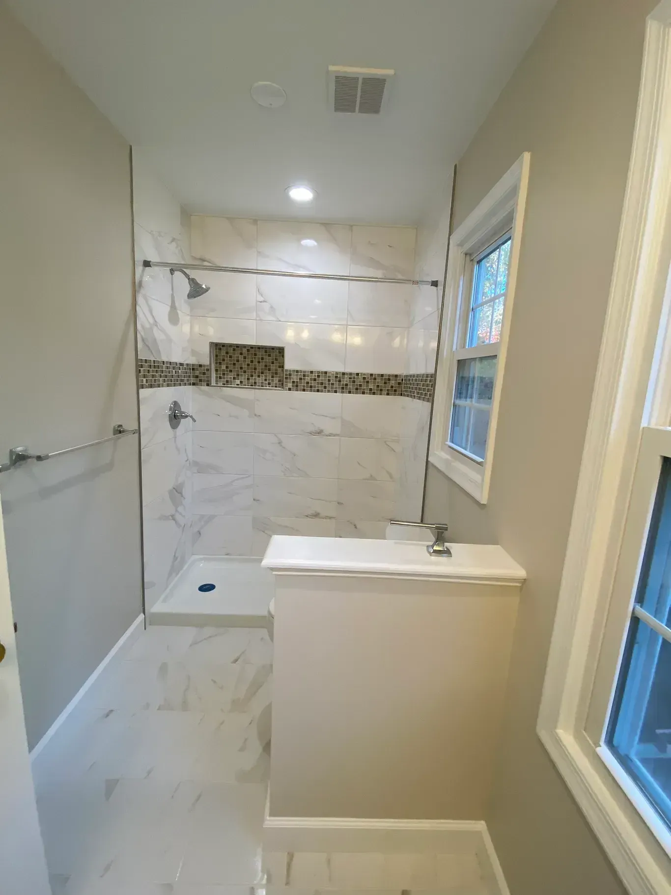 A bathroom with a walk in shower , sink , and window.
