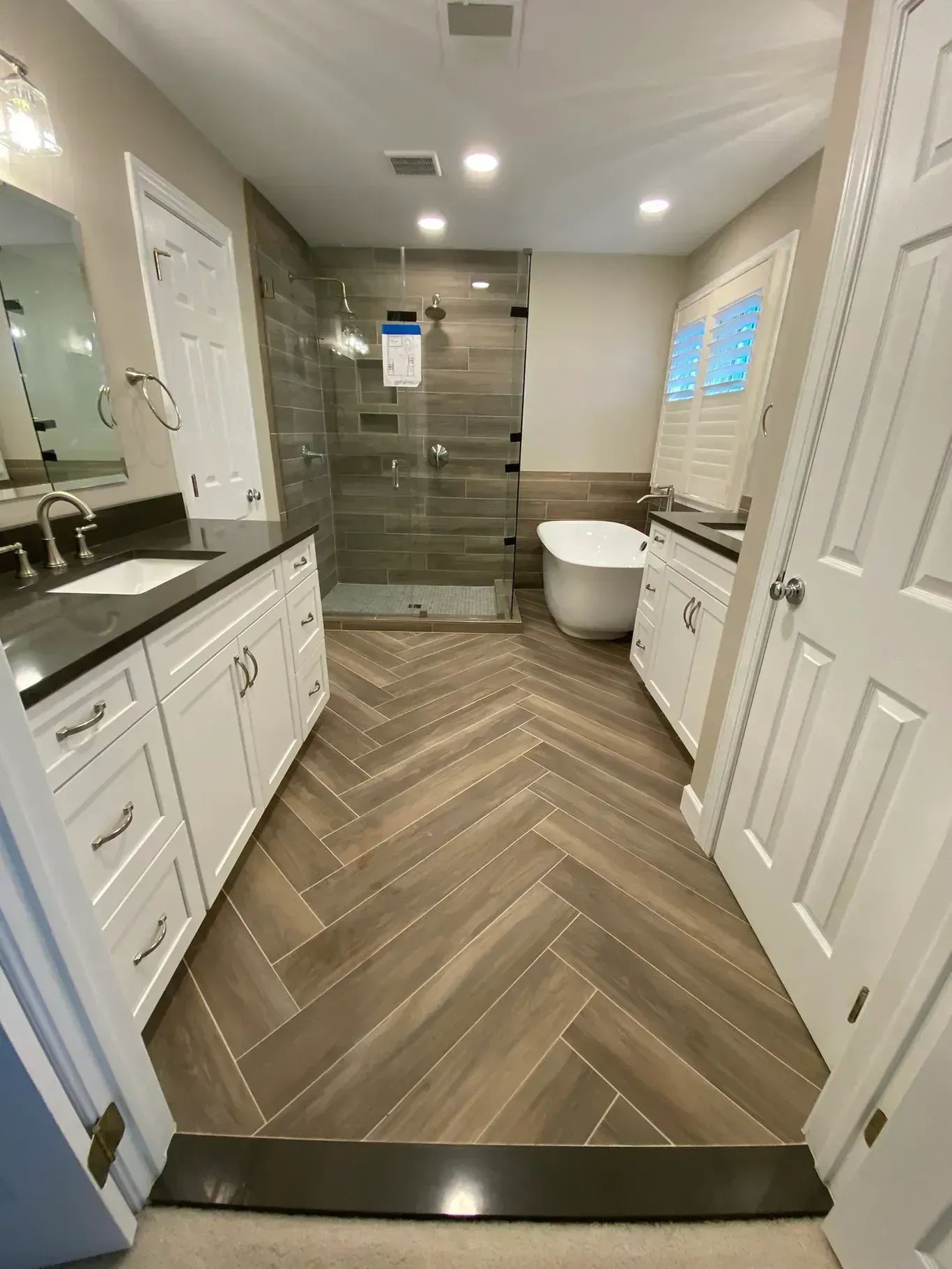 Narrow modern bathroom with herringbone wood floor, glass shower, white vanity, and toilet.