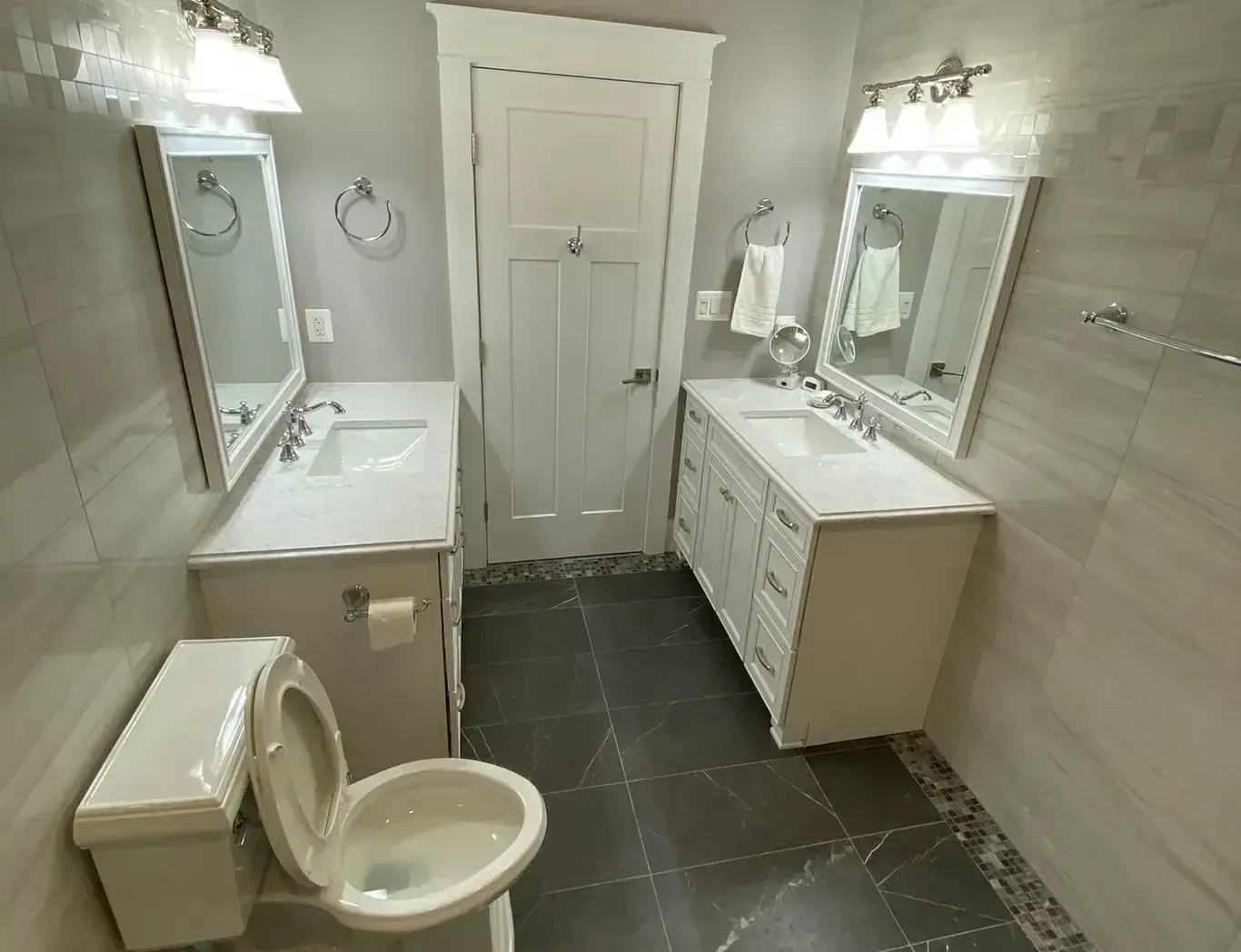 A bathroom with two sinks , a toilet , and two mirrors.
