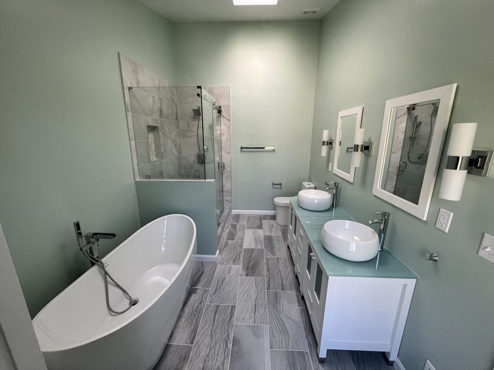 A modern bathroom with sage green walls, a white soaking tub, double vanity with vessel sinks, and a glass-enclosed shower.