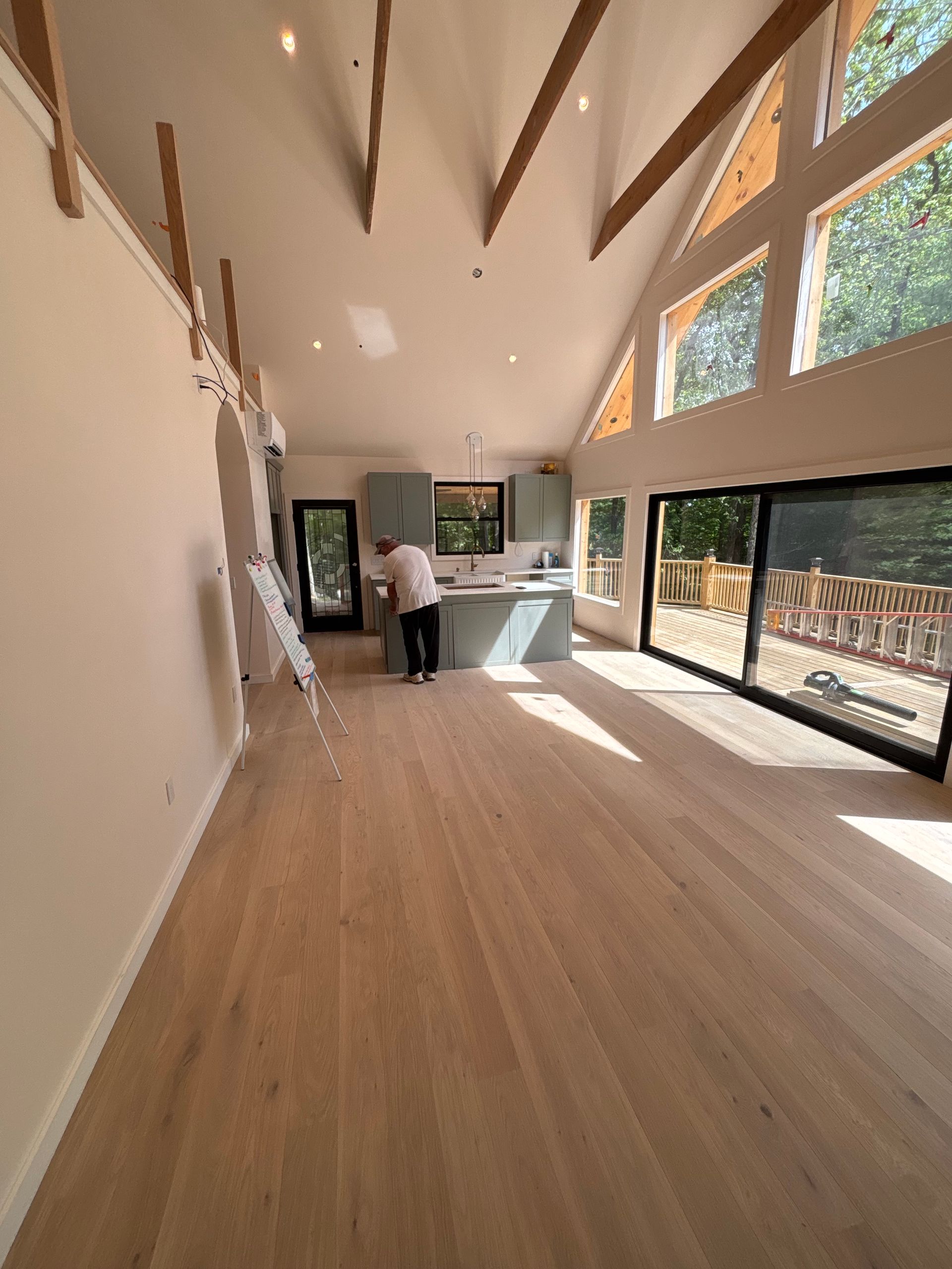 Bright modern room with wood floor, tall windows, and a person standing by the kitchen island.