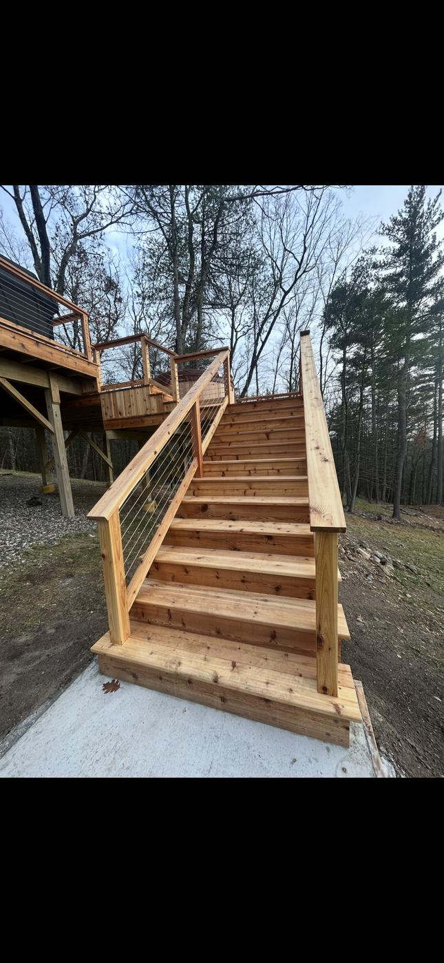 Wooden outdoor staircase with railings leading up a deck in a wooded yard