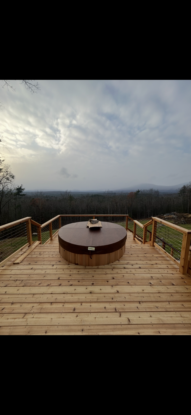 Wooden deck with round fire pit overlooking a misty valley under a cloudy sky