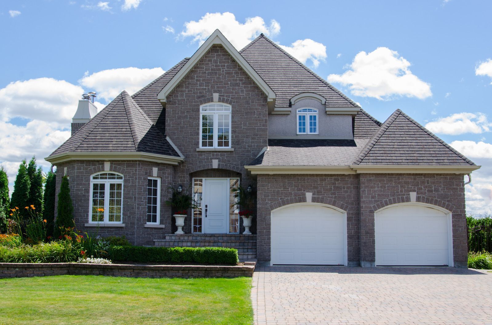 A large brick house with three white garage doors and a driveway.