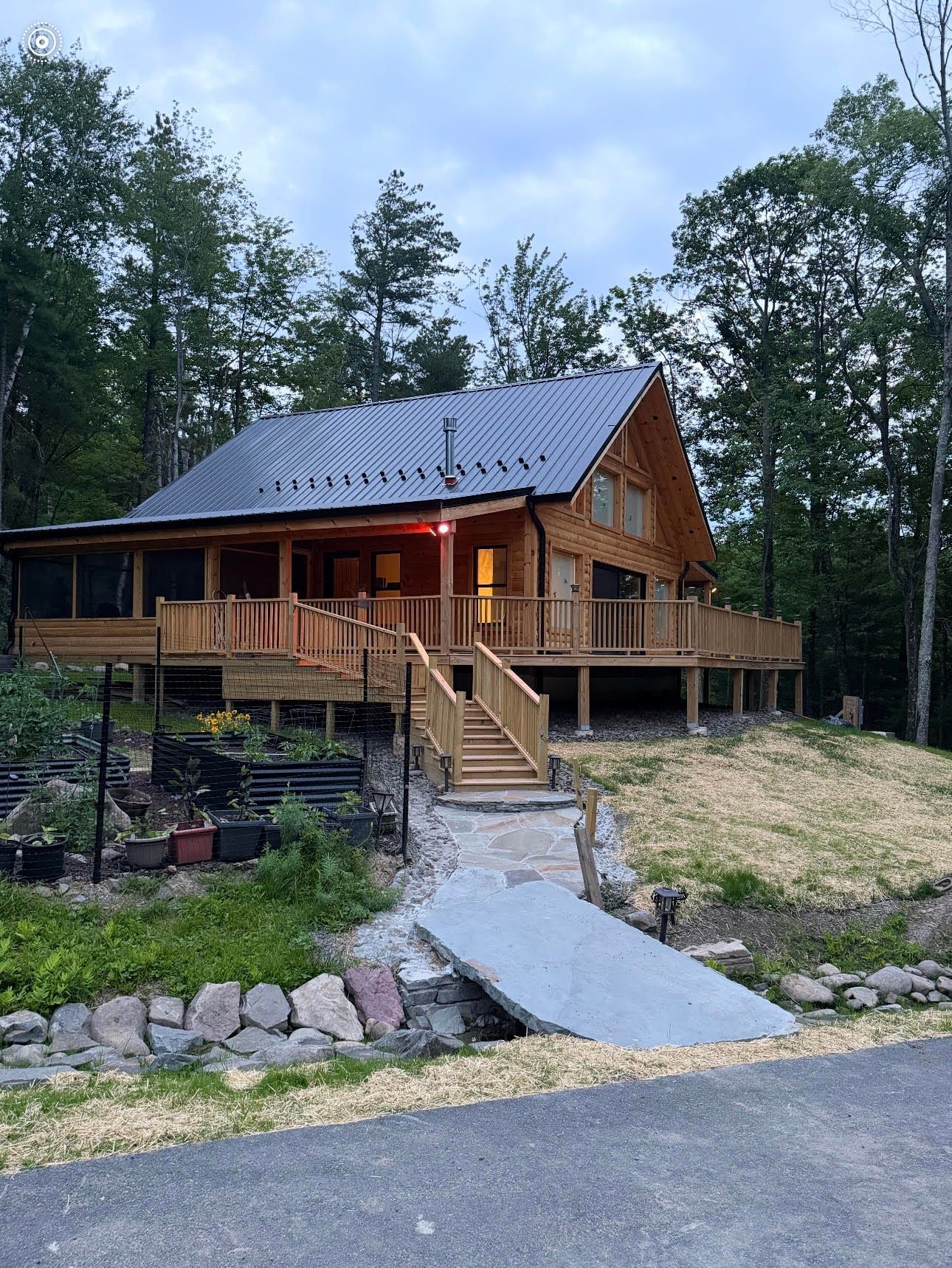 Wooden cabin with porch and front steps on a wooded hillside at dusk