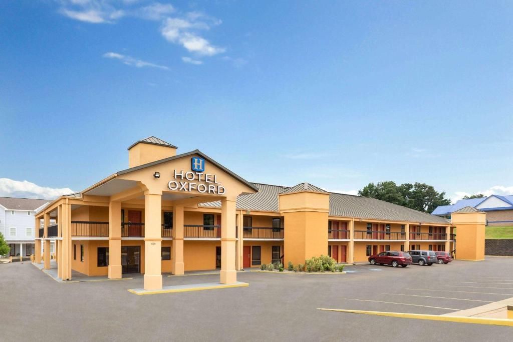 Orange motel building with entrance canopy under a blue sky, parking lot in front.