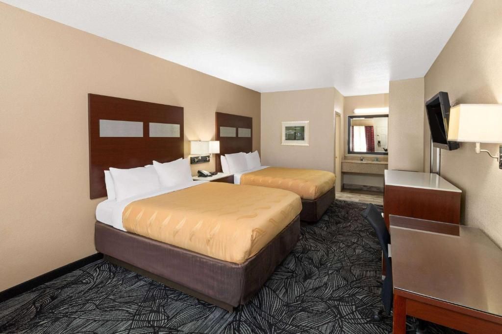 Hotel room with two beds, dresser, and bathroom visible. Beige and dark brown colors.