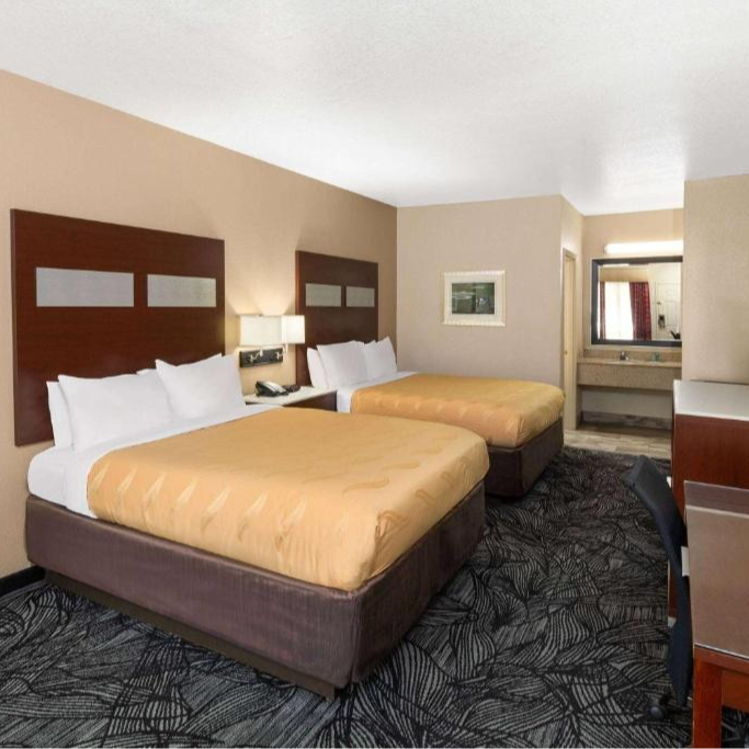 Hotel room with two queen beds, beige walls, and bathroom visible in the background.