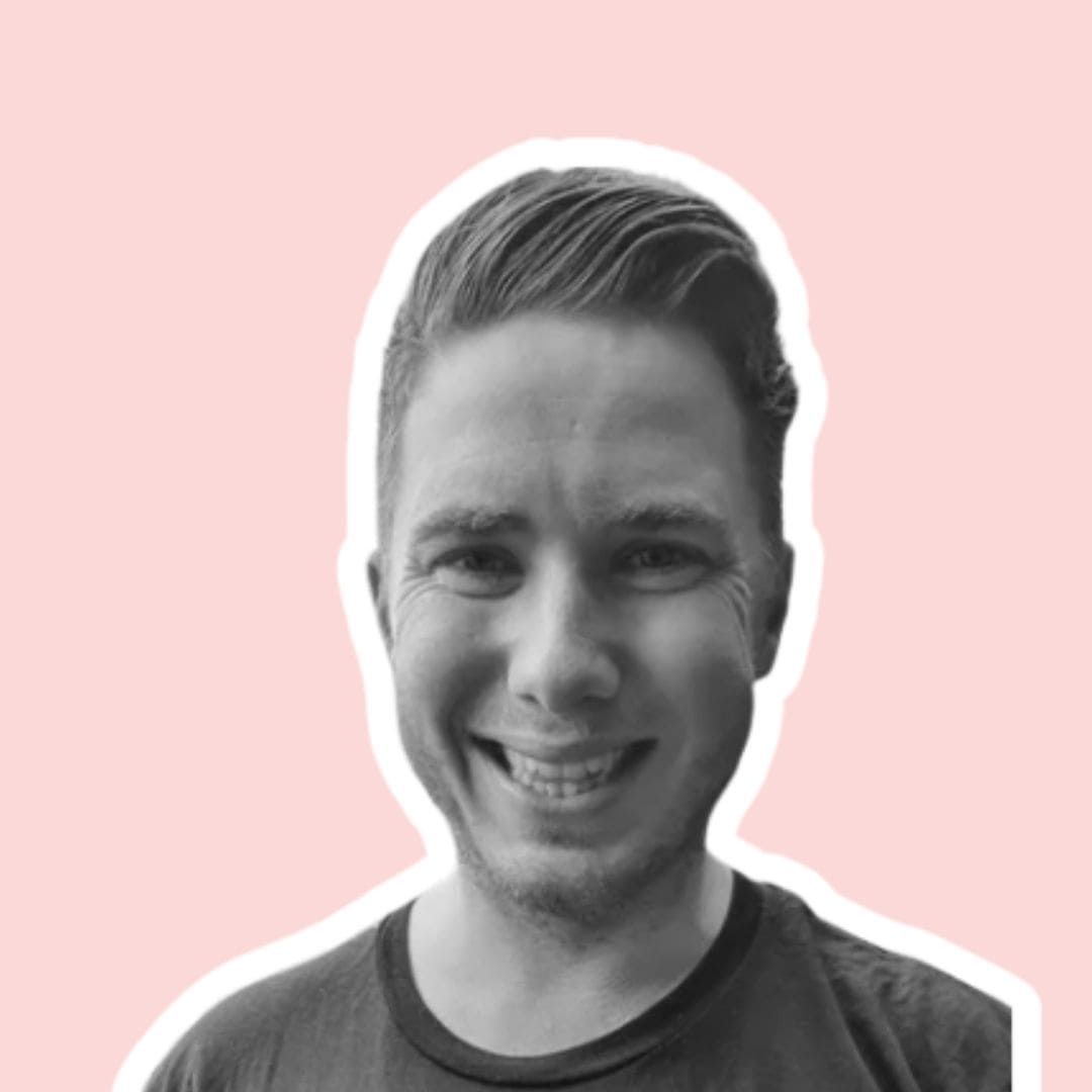 Harry Hillis with styled hair in a black crew-neck shirt against a solid light pink background.